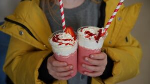Dva milkšejka od jagode sa šlagom i prelivom u rukama gosta na Danima sladoleda